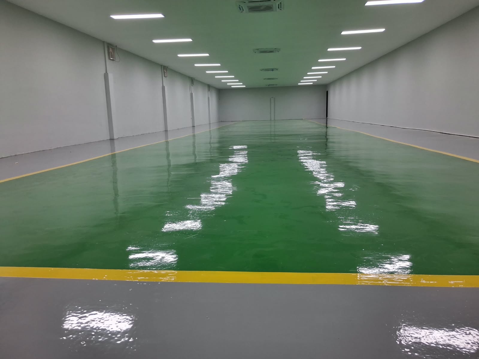 Lantai epoxy hijau mengkilap pada ruang produksi industri dengan marka kuning