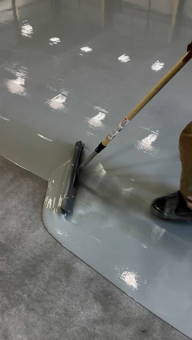 Pekerja meratakan cairan epoxy abu-abu dengan squeegee